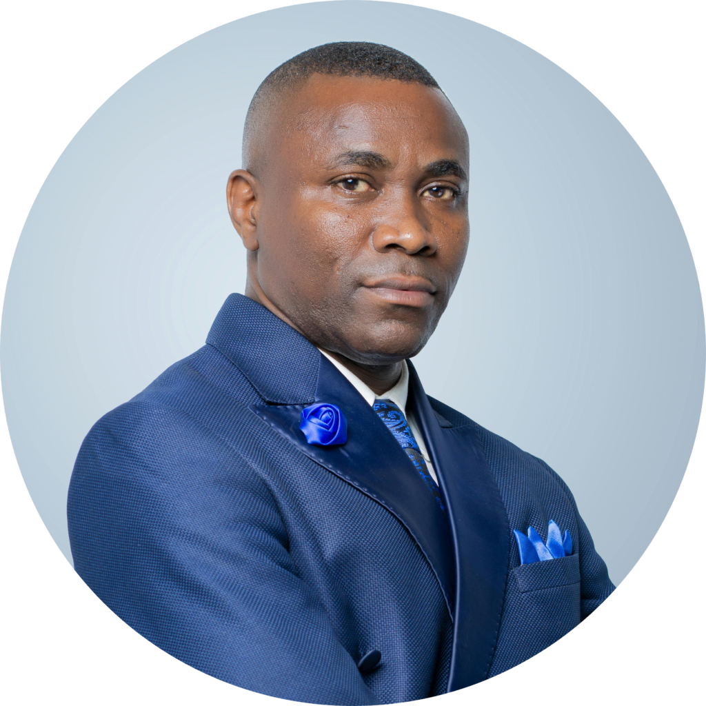 A polished man in a navy suit with a blue flower lapel pin, standing confidently against a soft gradient background.