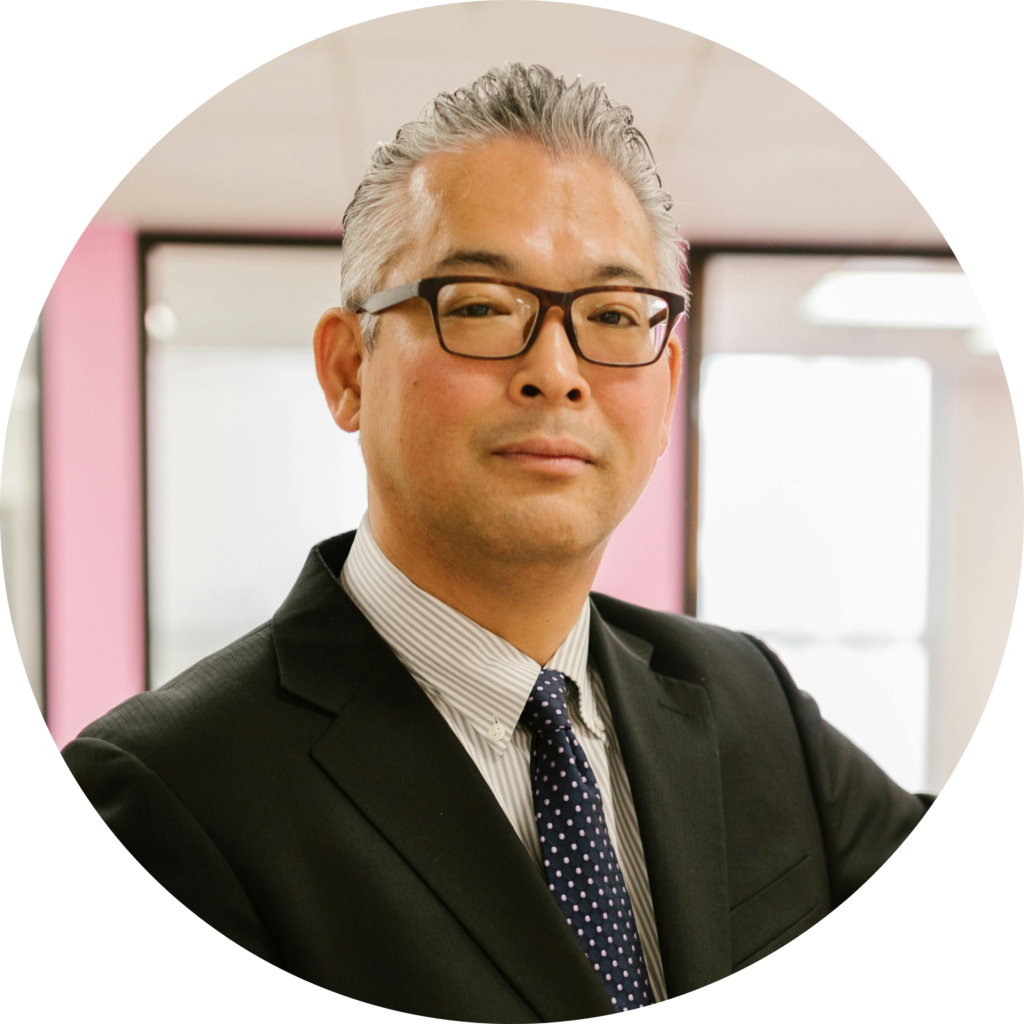 A professionally dressed man in a suit and tie stands confidently in a modern office space with bright pink accents.