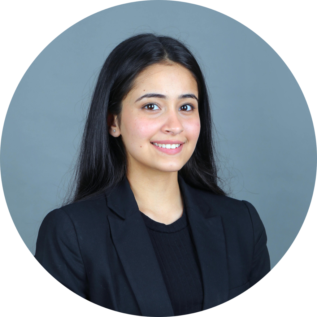 Professional young woman with long black hair in black blazer smiling against gray background, business headshot